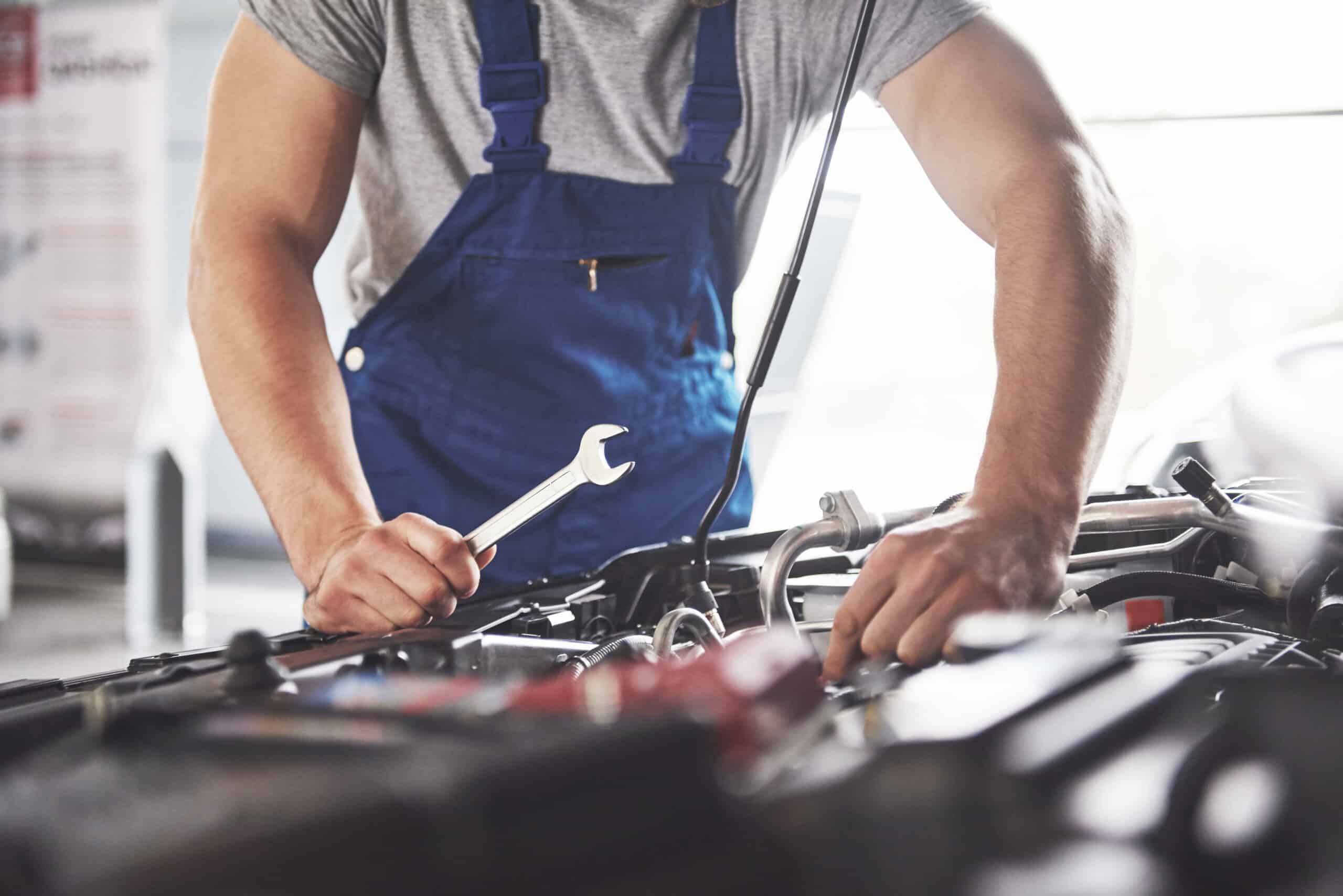 homme réparant moteur d'une voiture capot ouvert.